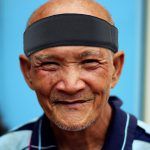 Wearing a black protective headband by Forcefield® on an elderly man with a joyful expression, close-up portrait.