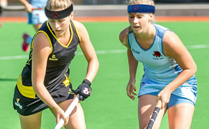 Two young female athletes wearing Forcefield® Protective Headbands during a field hockey game, demonstrating safety and protection in non-collision sports.